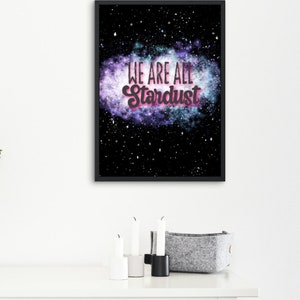 Peut inclure: Une impression encadrée noire avec un fond de galaxie et le texte "We are all Stardust" en rose et blanc.