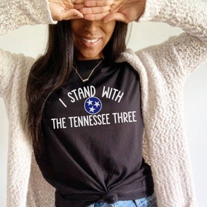 May include: Black t-shirt with white text that reads "I Stand With The Tennessee Three" and a blue and white star graphic.