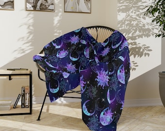 May include: A soft, purple and blue throw blanket with a repeating pattern of suns and moons. The blanket is draped over a wicker chair in a room with hardwood floors.