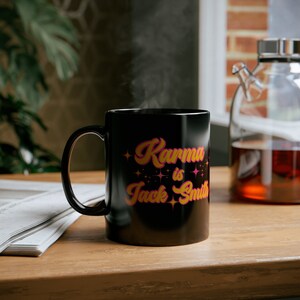 May include: Black ceramic coffee mug with a pink and yellow design that says "Karma is Jack Smith".