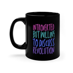May include: Black coffee mug with white text that reads "Introverted but willing to discuss revolution". The text is in different colors of pink, blue, and teal.