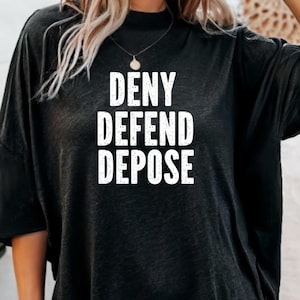 May include: Black oversized t-shirt with the text "DENY DEFEND DEPOSE" printed in white.