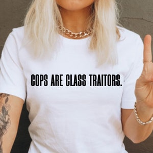 May include: A white t-shirt with the text "COPS ARE CLASS TRAITORS." printed in black.