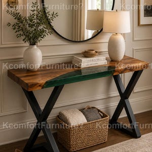 May include: A rectangular console table with a natural wood grain top featuring a translucent green resin inlay, supported by black metal X-shaped legs. The table holds a white vase with greenery, a stack of books, and a white table lamp.