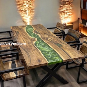 May include: A large wooden dining table with a green epoxy river running down the center. The table has a black metal base and is surrounded by six black metal chairs.