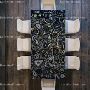 May include: Overhead view of a rectangular dining table with a dark blue and gray agate stone top. The table is surrounded by eight cream-colored upholstered chairs. The table and chairs are set on a dark wood floor.