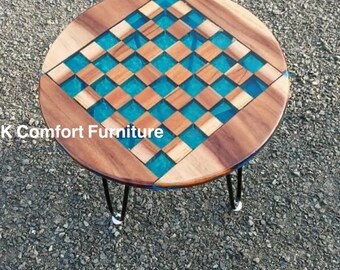 Op de afbeelding: Ronde houten tafel met een turquoise en houten geruit tafelblad. De tafel heeft zwarte haarspeldpoten. De tafel heeft een diameter van ongeveer 61 cm.