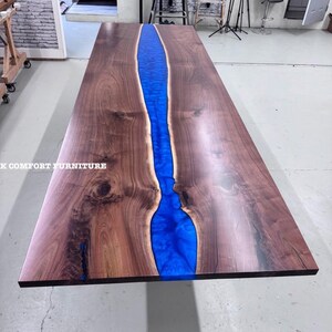 Puede incluir: Una mesa de madera rectangular grande con un río de resina azul vibrante en el centro. La madera tiene un color marrón oscuro intenso con vetas visibles. Una pieza de mobiliario llamativa.