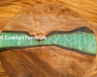May include: A round wooden table top with a green epoxy river design. The table top is made of wood with a natural wood grain. The epoxy river is a light green colour with a swirl pattern. The table top is approximately 45 cm in diameter. The text "K Comfort Furniture" is visible on the table top.