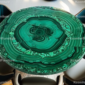 Op de afbeelding: Een ronde tafel met een levendig groen malachietblad, omringd door vier stoelen. De stoelen hebben teal-kleurige rugleuningen en lichtgekleurde zittingen. Het tafelblad heeft een uniek, concentrisch patroon. De stoelen hebben houten poten.