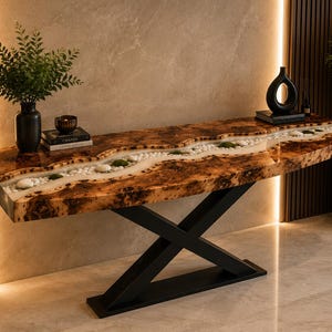 May include: A console table featuring a live-edge wood slab with a central river-like inlay filled with white river stones and green moss, encased in clear resin. The table is supported by a black metal X-shaped base with a flat rectangular foot.