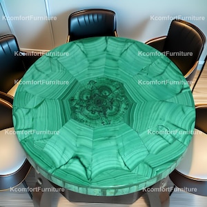 Op de afbeelding: Een ronde tafel met een levendig groen malachietblad, met een uniek patroon van wervelende lijnen en vormen. De tafel is omringd door zwarte leren stoelen, wat een luxe en stijlvolle eethoek creëert.