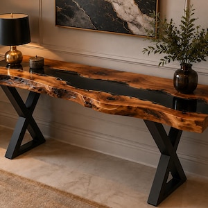May include: A long console table featuring a natural live-edge wood slab with a central black resin river inlay. The table is supported by two black metal X-shaped legs. A black lamp and a dark vase with green foliage sit on the wood surface.