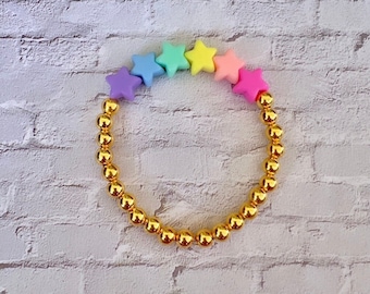 Peut inclure: Un bracelet en perles dorées avec des perles en forme d'étoile arc-en-ciel pastel.