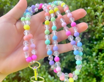 May include: A rainbow beaded lanyard with a silver key ring. The lanyard is made of pastel colored beads and clear crystal beads.