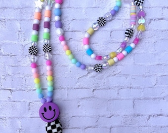 May include: A colorful beaded lanyard with a purple smiley face charm and a black and white checkered bead. The lanyard is made with pastel colored beads, including pink, blue, yellow, and green. The lanyard has a silver clasp.