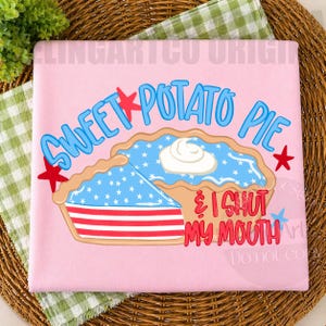 May include: Pink t-shirt featuring a graphic of a sweet potato pie with a slice cut out. The pie has a blue filling with white stars and a dollop of whipped cream. Text reads "SWEET POTATO PIE & I SHUT MY MOUTH."