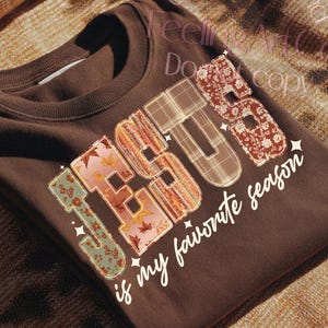 May include: A folded brown t-shirt with the word "JESUS" in a patchwork design, featuring floral, plaid, and leaf patterns. The phrase "is my favourite season" is printed below in white script. The shirt is a digital download.