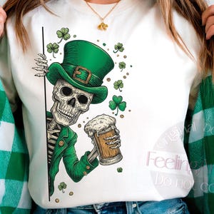 Op de afbeelding: Witte crewneck sweatshirt met een skelet met een groene kaboutermuts en jas, met een bierpul. Het ontwerp bevat klavers, perfect voor St. Patrick's Day.