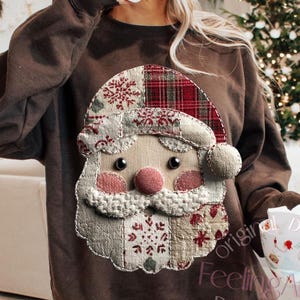 Könnte beinhalten: Ein braunes Sweatshirt mit einem Santa Claus-Applikation, mit rotem Schottenmuster-Hut und rosa Nase. Der Santa besteht aus Stoffflicken. Der Text "Feeling Art Co" und "Do not copy" ist auf einem Becher zu sehen.