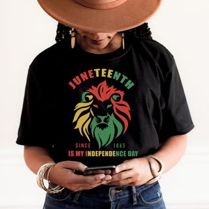 May include: A black t-shirt with a graphic of a lion's head in red, yellow, and green colors. The text "Juneteenth Since 1865 Is My Independence Day" is printed on the shirt.