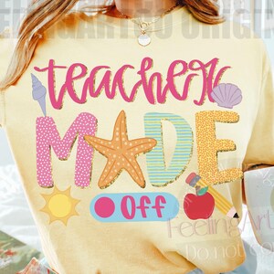 May include: Yellow t-shirt with the words "Teacher Made Off" in colorful, beach-themed letters and graphics. The design includes a seashell, starfish, sun, apple, and pencil. A white mug with a smiley face is held in the hand.