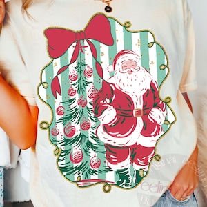 May include: Cream-colored t-shirt featuring a Christmas design. The design includes a red bow, a Christmas tree with ornaments, and Santa Claus in a red suit. The design is framed by a green and gold border.