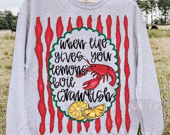 May include: A heather gray sweatshirt with a design featuring the text "When life gives you lemons, boil crawfish." The design includes a red crawfish, lemon slices, and red vertical stripes.