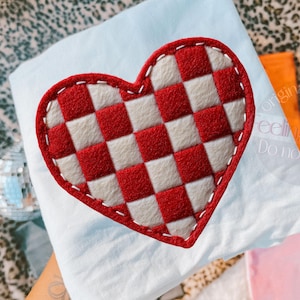 May include: A red and white checkered heart-shaped applique with a white stitched border. The applique is on a light blue fabric. The image also includes a disco ball, and other colorful items.