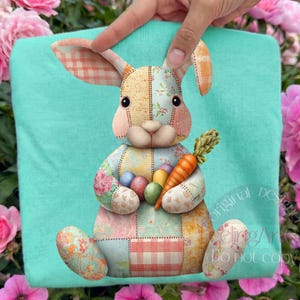 Puede incluir: Una sudadera turquesa con un diseño de conejo de retazos que sostiene una zanahoria y huevos de Pascua. El conejo está hecho de varias telas estampadas. El diseño incluye el texto "Original Design" y "Do not copy".