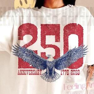 Puede incluir: Camiseta blanca con un gráfico rojo desgastado "250" y una ilustración de águila azul y blanca. El texto "ANNIVERSARY 1776 2026" está debajo del águila. La camiseta tiene mangas cortas.