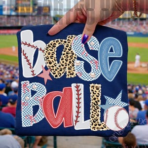 Peut inclure: T-shirt bleu marine sur le thème du baseball avec le mot "baseball" dans un mélange de motifs et de couleurs. Les lettres sont blanches, rouges, bleues et imprimées léopard. Un graphisme de baseball est également inclus.