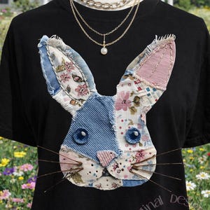May include: Black t-shirt featuring a patchwork bunny face with denim, floral, and pink fabric details. The bunny has blue button eyes and wire whiskers. The shirt also has text that says "original design FeelingArt Do not copy."