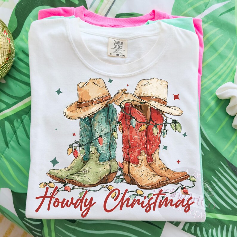 May include: White t-shirt with a graphic of cowboy boots and hats decorated with Christmas lights. The boots are green and red, and the hats are tan. The text "Howdy Christmas" is written in red script below the boots.