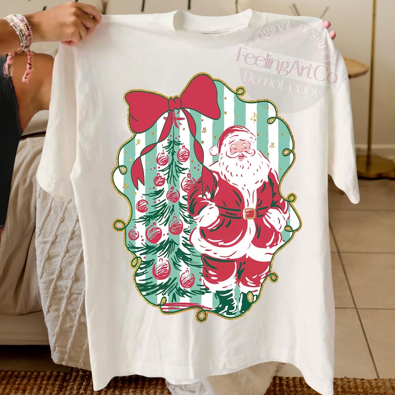 May include: White t-shirt featuring a Christmas design. The graphic includes Santa Claus in a red suit, a Christmas tree with red ornaments, and a large red bow. The design is framed with a gold border and the text "FeelingArtCo Do not copy".