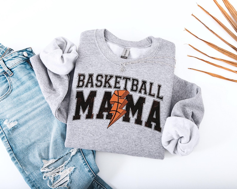 May include: Gray sweatshirt with the text "Basketball Mama" in black and orange lettering. A basketball with a lightning bolt is in the center of the text.