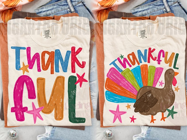 May include: Two cream-colored t-shirts featuring colorful graphic designs. The left shirt displays the word THANKFUL in multi-colored, distressed-style lettering with small stars. The right shirt shows the word THANKFUL above a brown turkey with a vibrant, multi-colored fan-shaped tail and small stars.