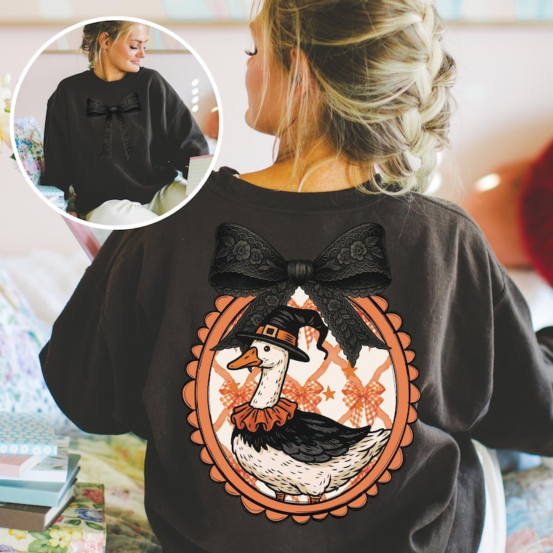 Peut inclure: Sweat-shirt gris fonc&eacute; avec un grand n&oelig;ud en dentelle noire au dos. Le sweat-shirt pr&eacute;sente un motif ovale avec une oie de dessin anim&eacute; portant un chapeau de sorci&egrave;re et un col &agrave; volants. L'avant du sweat-shirt a un petit n&oelig;ud noir.