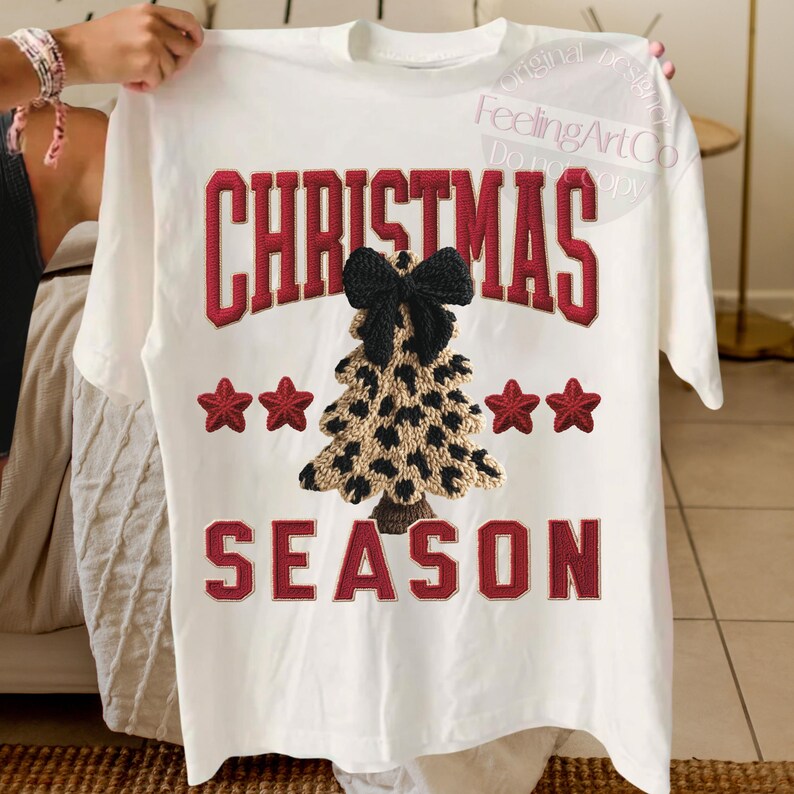 May include: White t-shirt with the words "CHRISTMAS SEASON" in red, outlined in white. A leopard print Christmas tree with a black bow is centered on the shirt, with red stars on either side.