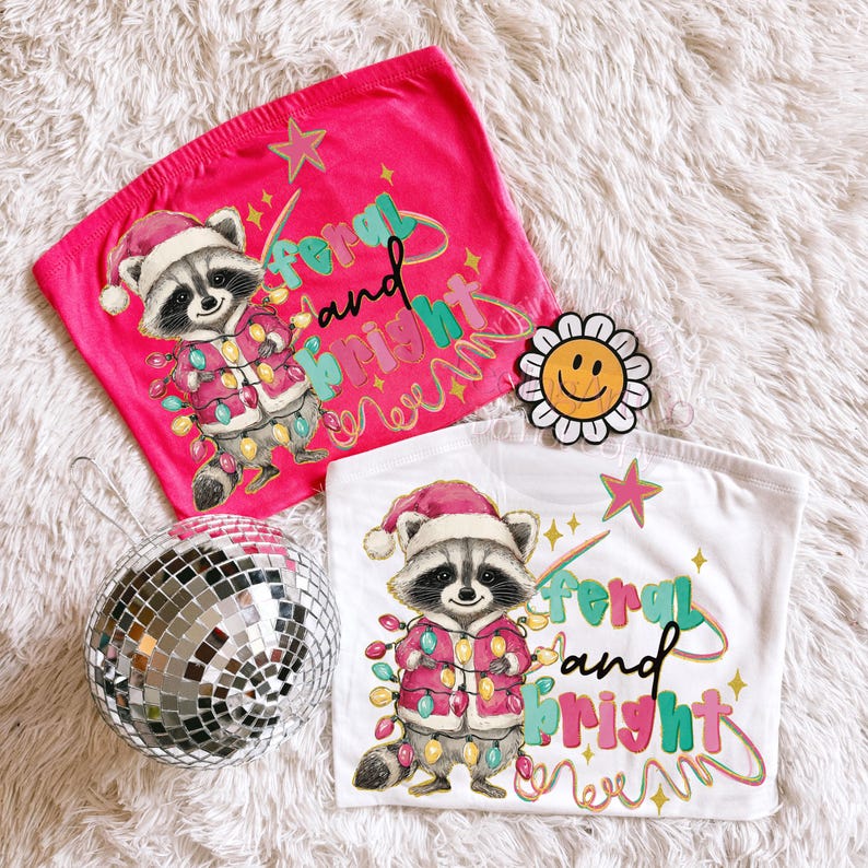 May include: Two tube tops, one pink and one white, with a raccoon wearing a Santa hat and Christmas lights. The text "Feral and Bright" is printed on the front. A disco ball and a daisy-shaped smiley face are also in the image.
