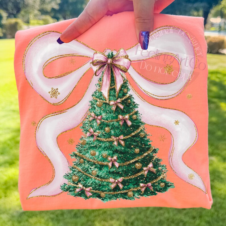 Pu&ograve; includere: Una maglietta color corallo con un motivo a forma di albero di Natale. L'albero &egrave; decorato con fiocchi rosa e ornamenti dorati, su un grande fiocco bianco con accenti dorati. Il testo "Feeling Art Co Do not copy" &egrave; visibile.