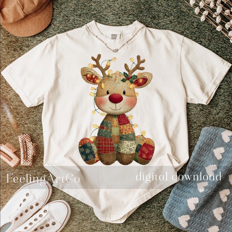 Puede incluir: Camiseta blanca con un dise&ntilde;o de reno con cuerpo de patchwork, cuernos y nariz roja. El reno est&aacute; adornado con luces de cadena. El texto "Feeling ArtCo" y "digital download" son visibles en la camiseta.