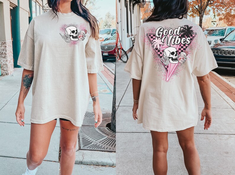 Puede incluir: Una camiseta beige de gran tama&ntilde;o con un gr&aacute;fico de calavera sosteniendo una bebida en la parte delantera y el texto "Good Vibes" con un gr&aacute;fico de calavera sosteniendo una bebida en la parte posterior.