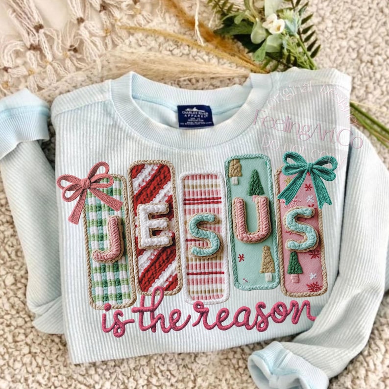 May include: Light blue sweatshirt with the words "JESUS is the reason" embroidered in pink. The letters are on decorative panels with various patterns and colors, including green plaid, red stripes, and pink with Christmas trees. A pink bow and a teal bow are on the panels.