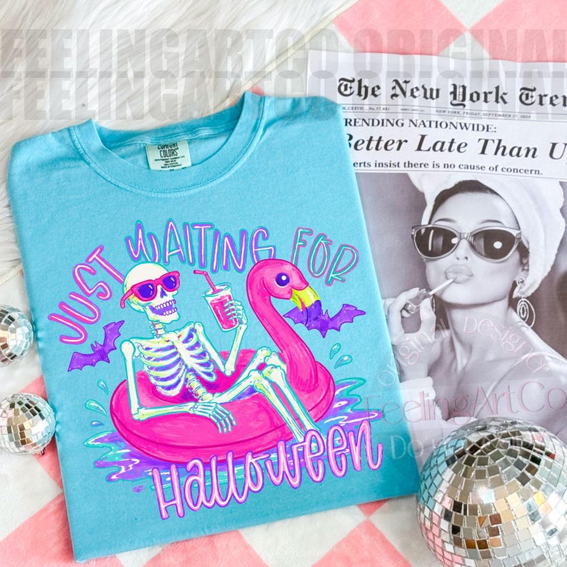 Peut inclure: Un t-shirt bleu clair avec l'inscription "Just Waiting For Halloween". Le graphisme repr&eacute;sente un squelette avec des lunettes de soleil, un flotteur flamant rose et des chauves-souris violettes. Le t-shirt est de la marque Comfort Colors.
