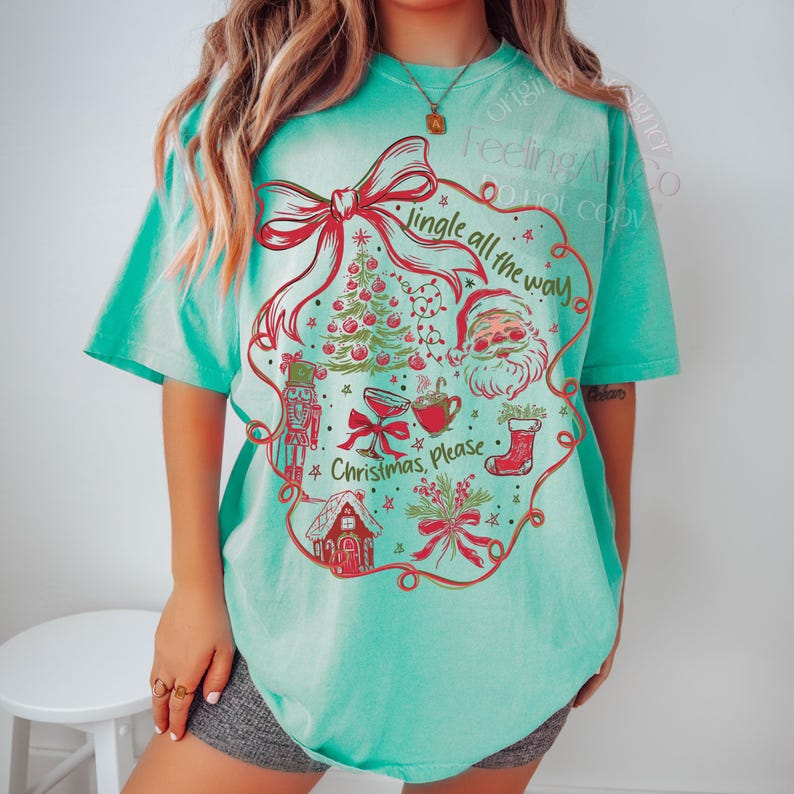 May include: A turquoise t-shirt with a festive Christmas design. The graphic includes a red bow, Christmas tree, Santa Claus, and the text "Jingle all the way" and "Christmas, please".