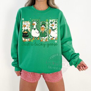 May include: Green sweatshirt with a St. Patrick's Day theme. The design features four cartoon geese in green outfits, with the text "Just a lucky goose". The geese are in rectangular frames with shamrock accents.