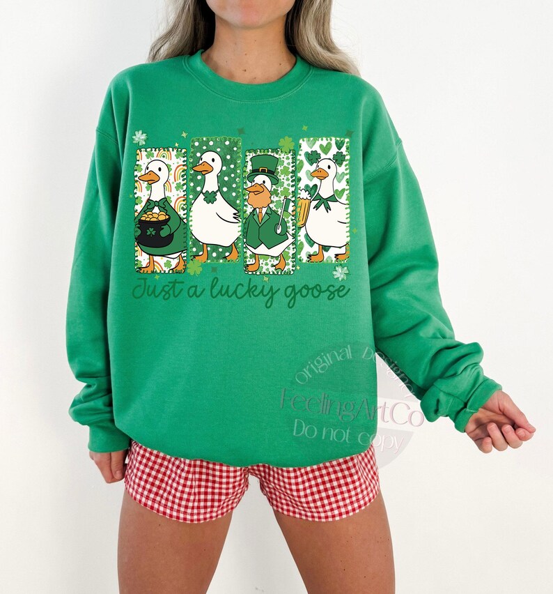 May include: Green sweatshirt with a St. Patrick's Day theme. The design features four cartoon geese in green outfits, with the text "Just a lucky goose". The geese are in rectangular frames with shamrock accents.