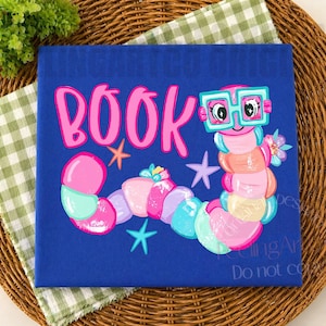 May include: A square blue sign featuring the pink text BOOK and a colorful cartoon worm wearing large teal glasses. The worm is composed of pink, peach, and teal segments, decorated with small flowers and surrounded by several teal and purple starfish.