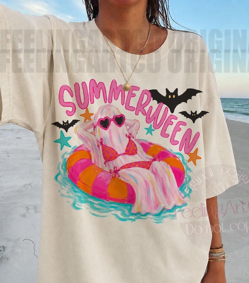 K&ouml;nnte beinhalten: Cremefarbenes T-Shirt mit einem "Summerween"-Motiv. Das Design zeigt einen Geist mit Sonnenbrille und Bikini, der in einem rosa-orangenen Schwimmring entspannt. Schwarze Flederm&auml;use und Sterne umgeben den Geist.